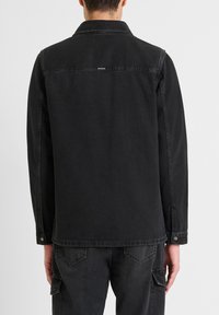 Zwarte denim jas met lange mouwen, een kraag en drukknopen aan de mouwen. Beschikt over een logo-label op de achterkant en een recht gesneden ontwerp.