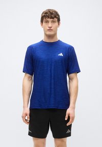 Modra športna majica s teksturiranim vzorcem, okroglim izrezom in kratkimi rokavi. Na zgornji levi strani je bel logotip Adidas.
