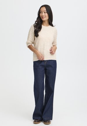 Beige knitted sweater with textured sleeves, paired with dark blue flared jeans and brown boots. Simple, cohesive outfit.