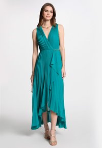 Robe plissée en teal avec un design enveloppant, décolleté en V et ourlet asymétrique. Présente une couche froncée et un accent en chaîne dorée à la taille.