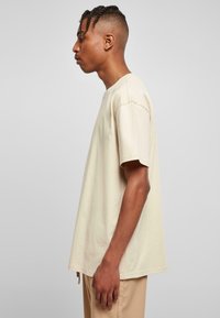Beige bomulls t-skjorte med korte ermer, rund hals og en avslappet passform. Synlige sømmer på skuldrene og sideslits for økt bevegelsesfrihet.