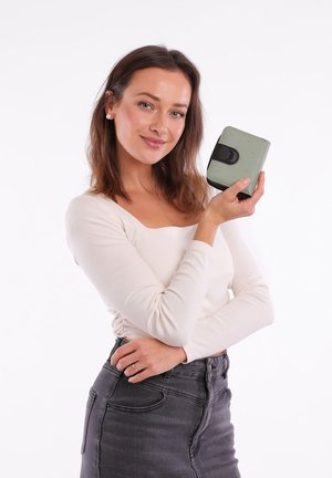 Compact square wallet in matte light green with raised dots, secured by a black strap. Textured surface, zip closure, and rounded corners.