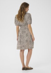 Robe à manches courtes en beige avec un motif à pois noirs. Caractéristiques : taille cintrée, jupe évasée et tissu doux et léger.