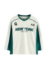 Košeľa s dlhým rukávom vyrobená z bielej tkaniny s akcentmi v tehlovej farbe. Obsahuje grafiku a textové detaily "NEW YORK". V-krčný dizajn s kontrastnými švami.