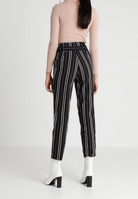 Svart- och vitrandiga högmidjade byxor med rak passform och bältesloopar, kombinerat med vita klackade ankelstövlar.