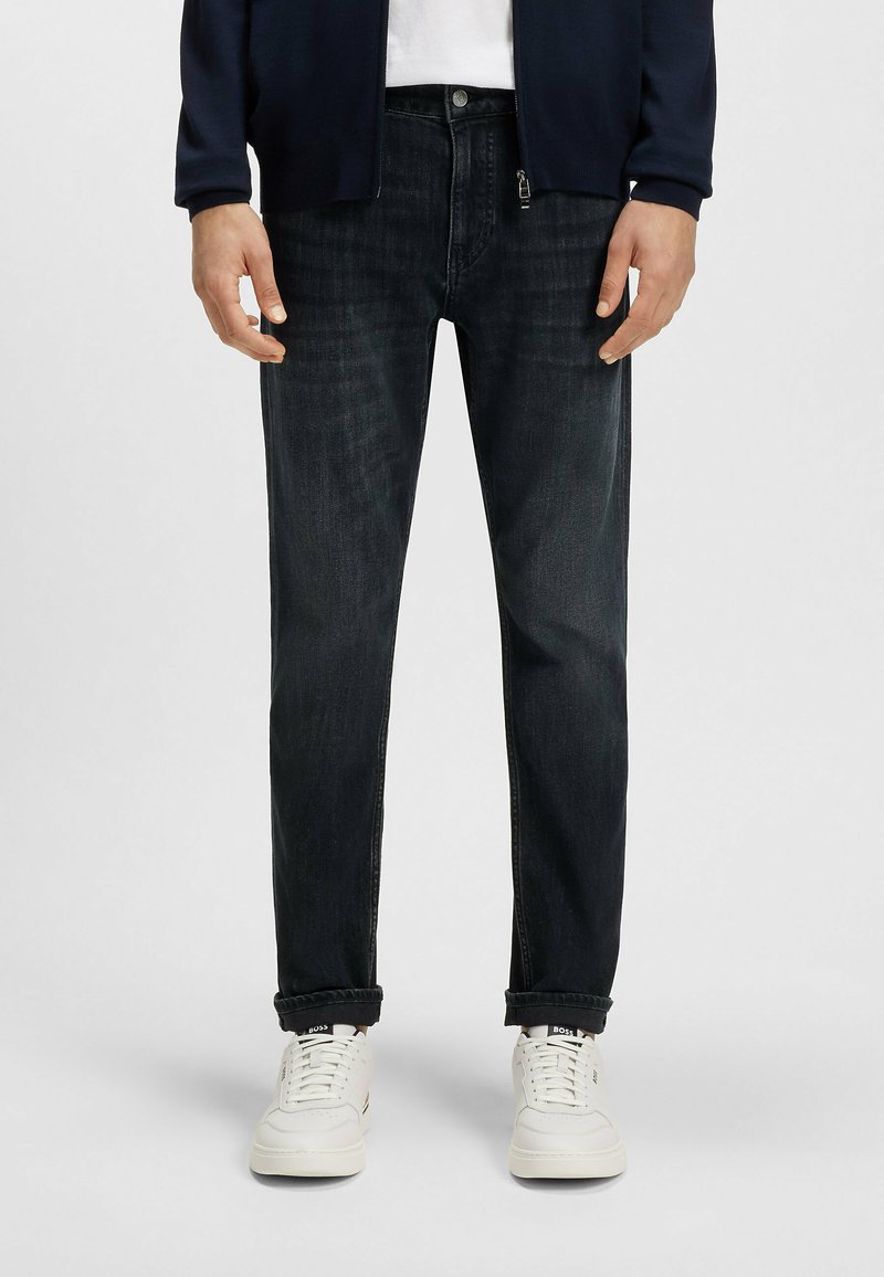 Ciemnoniebieskie dżinsy z prostymi nogawkami, z zapięciem na guzik, subtelnym przetarciem oraz pięcioma kieszeniami, w komplecie z białymi trampkami.