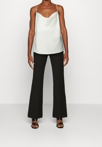 Vaaleanharmaa satiininen toppi, jossa on V-pääntie, yhdistettynä mustiin valtavatsaisiin housuihin ja mustiin avokärkisiin korkokenkiin. Pinnassa on sileä tekstuuri.