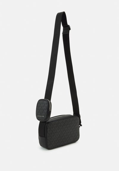Sac à bandoulière noir avec strap ajustable, présentant un motif monogrammé texturé et des accents en cuir lisse. Comprend une poche zippée à l'avant.