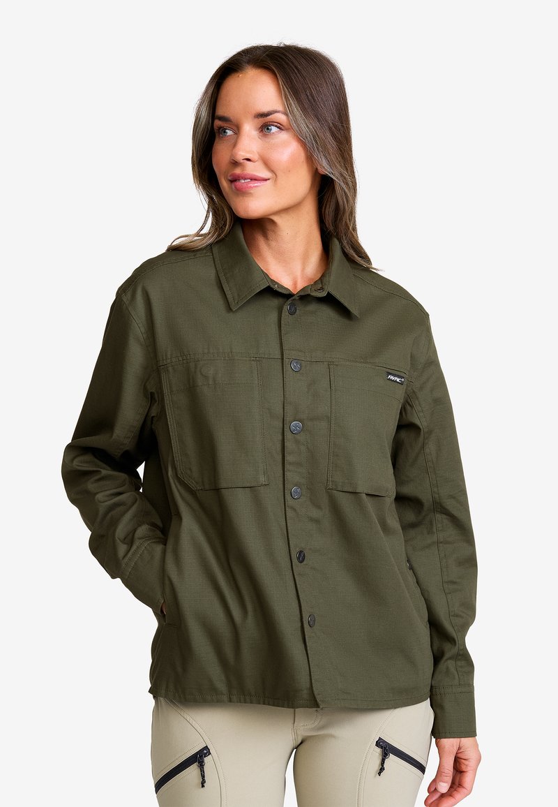 Olivgrön skjorta med knappar, två bröstfickor, långa ärmar och en strukturerad krage. Tillverkad av slitstarkt tyg med en slät yta.