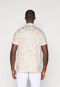 Beige Polohemd mit kurzen Ärmeln, das ein abstraktes weißes Wellenmuster, eine glatte Textur und einen Kragen hat.