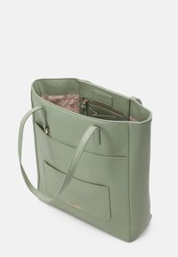 Sac fourre-tout en simili cuir vert avec double poignées, ouverture supérieure, poche avant et doublure intérieure rose arborant un motif logo subtil.