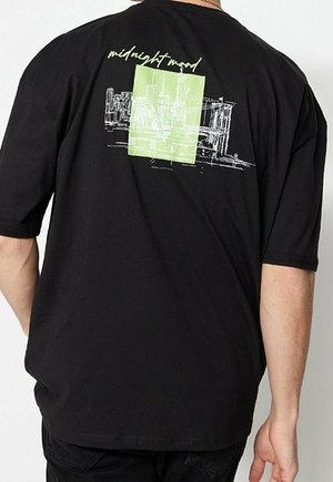 T-shirt nera con schizzo bianco della skyline di New York, che include la Statua della Libertà e il Ponte di Brooklyn, e un rettangolo verde dietro il design.