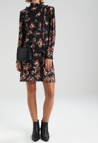 Vestido negro de flores con mangas largas, escote alto y estampado floral. Combinado con un bolso negro bandolera y botas negras hasta los tobillos.