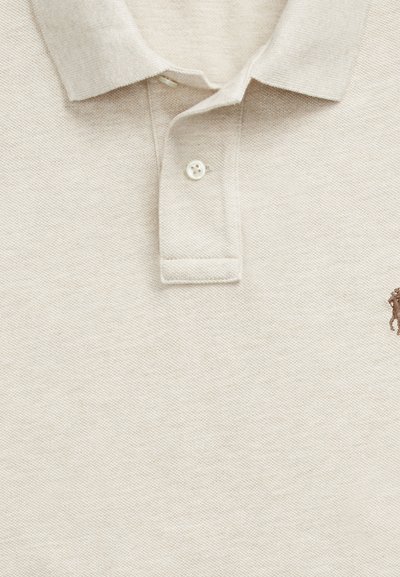 Bež teksturirana polo majica z rebrastim ovratnikom, dvema gumboma na bridki in delno vezenim logotipom na desni strani.