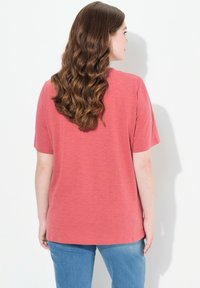 Camiseta de manga corta en color coral, fabricada en un tejido suave y texturizado. Presenta un corte relajado, con escote redondo y dobladillo recto.