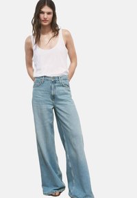 Vaqueros de pierna ancha azul claro con cintura alta, combinados con una blusa sin mangas blanca. El denim presenta una textura suave y desgastada y detalles de costura mínimos.