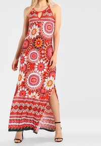 Vestido maxi en un vibrante rojo, con patrones florales y un diseño de escote en forma de llave. Hecho de una tela ligera, con una abertura lateral. Acentuado por sandalias negras.