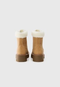 Bottes chelsea en cuir brun avec un rembourrage en fausse fourrure blanche. Semelle en caoutchouc épaisse avec un motif de sculpture visible et des détails de surpiqûres contrastants.