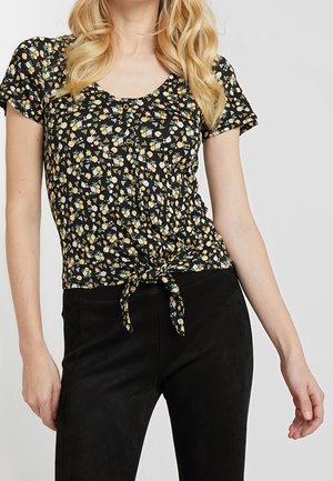 Top estampado floral negro con mangas cortas, cuello redondo, botones delanteros y detalle de lazo en la cintura. Combinado con pantalones negros.