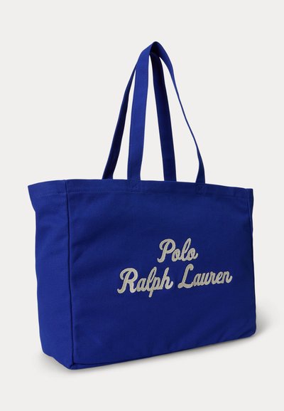 Τσάντα ώμου από μπλε καμβά με δύο λαβές, με λευκή κεντημένη επιγραφή "Polo Ralph Lauren" στο μπροστινό μέρος.