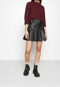 Burgundský pletený svetr s tříčtvrtečními rukávy, spárovaný s černou koženou sukní s rozšířeným lemem, která má kapsy a zip. Černé kotníčkové boty.