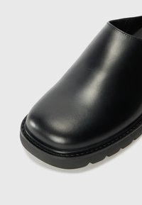 Svart skinnsko med glatt overflate, rund tå og tykk svart gummisåle. Enkelt design, ingen synlig maskinvare eller mønstre.
