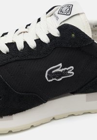Black suede and mesh sneaker with white laces. Features a prominent white embroidered logo, textured panel, and a light-colored outsole.