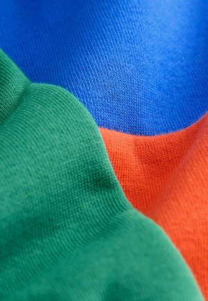 Nahaufnahme eines bunten Stoffes mit Abschnitten aus grünem, blauem und orangefarbenem Strickmaterial, das unterschiedliche Texturen und Webmuster zeigt.