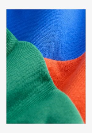 Close-up van kleurrijke stof met delen in groen, blauw en oranje gebreide materialen, die verschillende texturen en weefpatronen tonen.