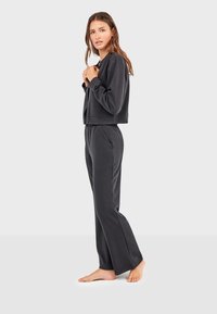 Dunkelgraue, langärmelige, cropped Jacke kombiniert mit lockeren, passenden Hosen. Weicher Stoff, lässiges Design, keine sichtbaren Verschlüsse oder Muster.