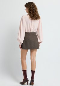 Blusa de color rosa claro con mangas abullonadas, combinada con una mini falda marrón, medias hasta la rodilla burdeos y zapatos de tacón marrones.