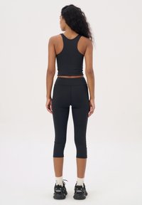 Zwarte sportieve crop top met een racerback ontwerp, gecombineerd met zwarte 3/4 leggings. Gladde textuur, nauwsluitende stijl en minimale naden.