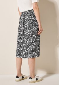 Gonna midi bianca e nera a fantasia con vita arricciata, abbinata a sneakers bianche con accenti neri e suole testurizzate.