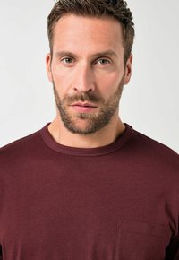 Bordeaux crew-neck t-shirt lavet af blødt stof, med en diskret brystlomme og en glat overflade. Ingen mønstre eller yderligere detaljer.