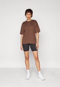 Pruun oversized t-särk lühikeste varrukatega, millel on väike logo; koos mustade rattapükste ja valgete tossudega.