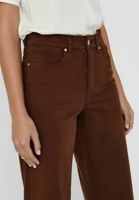 Bruine hoog-waist jeans van zacht denim, met vijf zakken, een knoopsluiting en zilveren hardware accenten. Gladde textuur, rechte pasvorm.