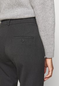 Pull en laine grise associé à un pantalon gris foncé ajusté avec une poche arrière ornée d'un bouton. Le tissu texturé semble lisse.