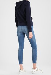 Felpa blu marina, jeans blu aderenti e sneakers bianche con dettagli dorati; i jeans presentano un orlo strappato e dettagli con zip.
