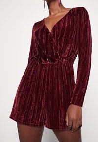 Burgundy sammet långärmad rompers med en djup V-ringning, midjeband och vertikal ribbad textur, med avslappnat passande shorts.