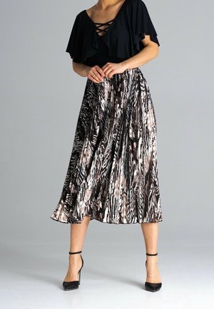 Mujer con blusa negra con volantes y hombros descubiertos, falda midi plisada con estampado animal, y tacones altos negros con tiras en el tobillo, de pie frente a un fondo gris.