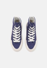 High-top sneakers in navy canvas, featuring white laces, a textured body, cream rubber soles, and rounded toes with stitched detailing.