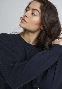 Marineblaues Sweatshirt aus weichem Stoff, mit langen Ärmeln und rundem Ausschnitt. Das Design umfasst dezente Stickdetails.