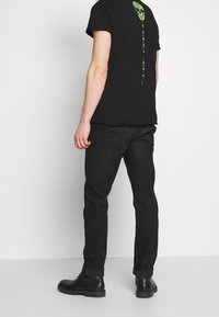 Svart T-shirt med en grön skalle-grafik på baksidan, tillsammans med svarta jeans och svarta snörstövlar. Enkel, figurnära design.