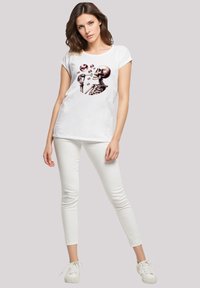 Weißes Baumwoll-T-Shirt mit einem Grafik eines Skeletts, das Seifenblasen macht. Kombiniert mit weißen Skinny-Jeans und weißen Turnschuhen.