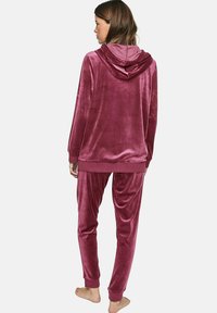 Ensemble de détente en peluche, rose profond, comprenant un haut à capuche et un pantalon fuselé. Texture douce avec des poignets et un ourlet en côtes.