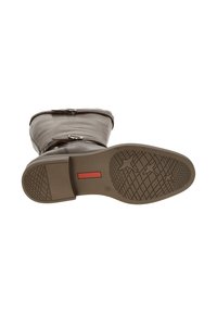 Bota de cuero marrón con puntera redondeada, detalles de hebilla lateral y suela de goma texturizada con un patrón de estrellas y detalle de logo rojo.