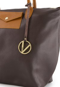Brun tekstureret læder tote taske med en tan flap og charm i guld-tone. Accentueret med brune håndtag og en blød suede rem.