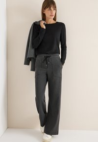 Pantalones anchos de color gris oscuro con un patrón texturizado, cinturilla elástica y cordón. Combinados con una camiseta de manga larga negra.