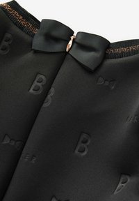 Czarna tkanina z wytłoczonymi literami i akcentem w postaci kokardy; posiada dekolt z prążkowanej tkaniny z dodatkiem złotych włókien oraz zamek błyskawiczny ukryty.