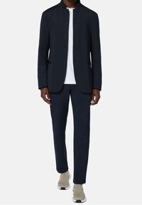 Marineblazer med hög krage och knäppning, matchad med slim-fit marinbyxor och beige sneakers, på en ljus bakgrund.